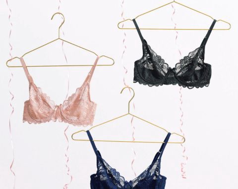 Three lace bras in pink, black, and navy hang on gold hangers.