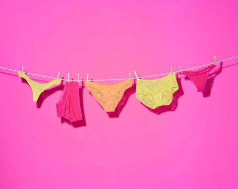 Colorful women's underwear hanging on a clothesline against a pink background.