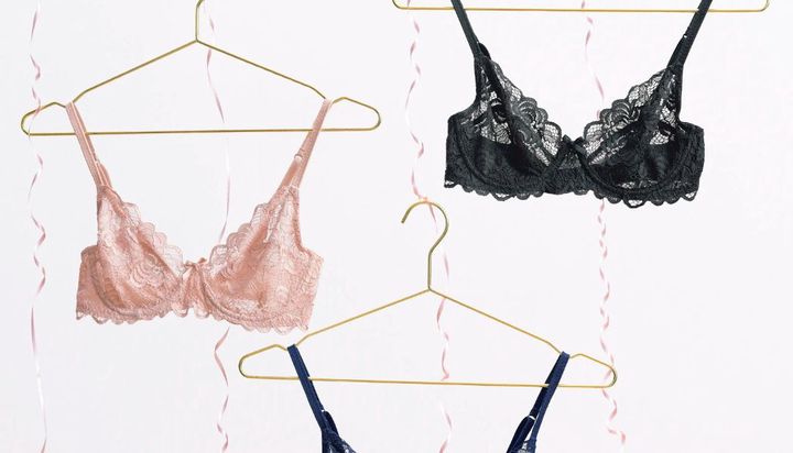 Pink, black, and blue lace bras hanging on gold hangers.
