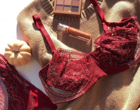 Lacy red bra and makeup products on a beige knitted sweater.