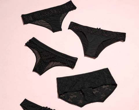 Four pairs of black lace women's underwear on a pink background.