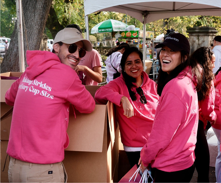 Three people in pink "Making Strides" hoodies smiling at an outdoor event.