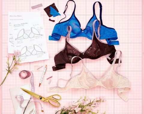 Three lace bras, sewing supplies, and bra sketches on a pink mat.