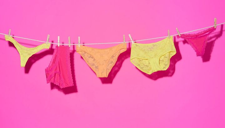Panties in various colors hanging on a clothesline against a pink background.