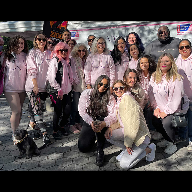 Group of people in pink hoodies with breast outlines, supporting breast cancer awareness.