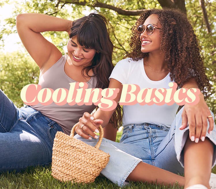 Two smiling women in "Cooling Basics" clothing sit on grass.