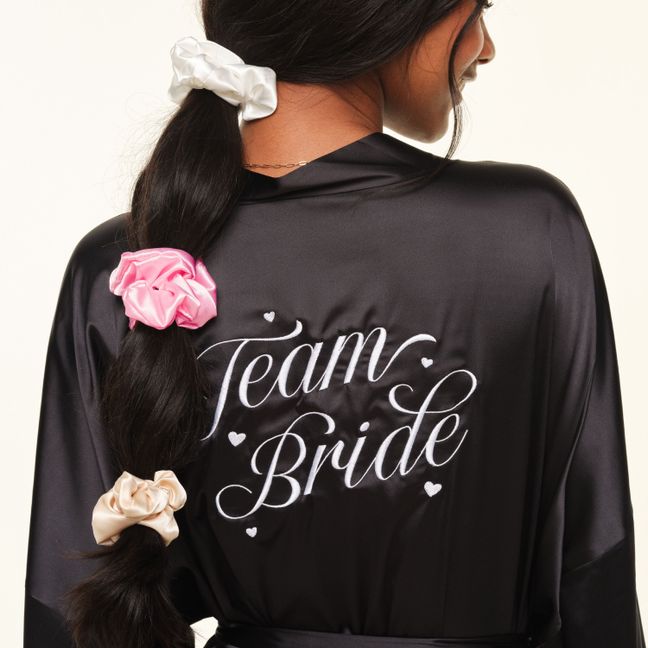 Black robe embroidered with "Team Bride" and scrunchies in hair.