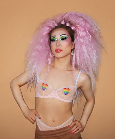Person with pink hair in sheer bra with rainbow heart pasties.